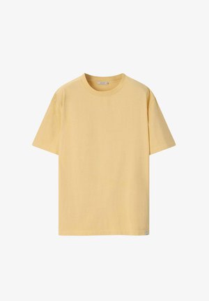 Effen gele katoenen T-shirt met korte mouwen, ronde hals en een klein labeltje bij de zoom, op een witte achtergrond.