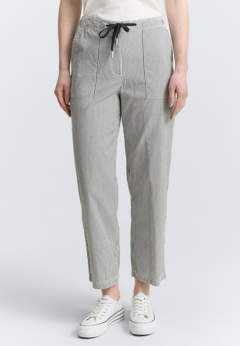 Pantalons en coton rayés avec une taille élastique et un cordon de serrage, dotés de poches avant et d'une coupe décontractée. Portés avec des baskets blanches.