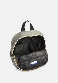 Zaino realizzato in tessuto grigio con una superficie liscia, presenta un interno nero, rifiniture in zip gialle e bianche, e una tasca inferiore con zip.