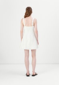 Weißes, ärmelloses Kleid mit tailliertem Oberteil und weit ausgestellt Rock. Verfügt über verstellbare Träger und einen gerafften Rücken für einen sicheren Sitz.