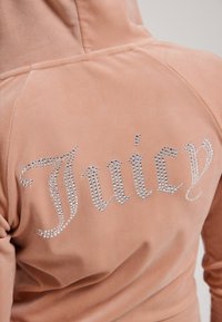 Felpa in velluto rosa con decorazioni in strass che formano la scritta "Juicy" sul retro. Tessuto morbido con una vestibilità relax e cappuccio.