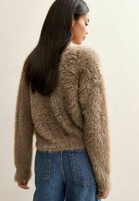 Braune Kunstfelljacke mit einem cropped Design, langen  Ärmeln und einer weichen Textur, kombiniert mit hochgeschnittenen blauen Jeans.