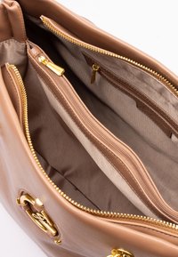 Interior de un bolso de piel color cuero con herrajes dorados, que cuenta con dos bolsillos con cremallera y un forro de tela suave.