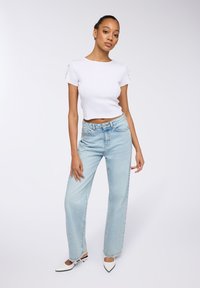 Top corto bianco a maniche corte abbinato a jeans a vita alta di colore azzurro chiaro e a gamba ampia. Modello con tacchi a punta bianchi con cinturino alla caviglia.