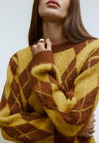 Gul- og brun diamantmønstret sweater med blød, struktureret stof og rund halsudskæring, der har lange ærmer og ribbede manchetter.