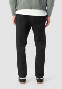 Sorte bukser med skræddersyet pasform, lavet af et glat stof, med et slip-on design og en subtil glans. Synlige sko accenter er lysebrune.