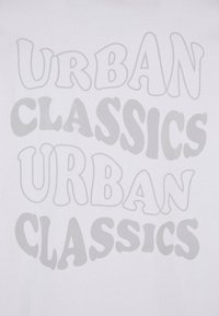 Balta T krekls ar lieliem, rotaļīgiem, pelēkiem burtiem, kas rakstīti ar tekstu "URBAN CLASSICS" dažādos izmēros un stilā, ar gludu kokvilnas tekstūru.