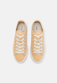 Sneakers in tela color tan con lacci bianchi, punta rotonda e suola in gomma. Presenta il logo Lacoste sul lato e un tessuto testurizzato.