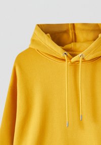 Sweat à capuche jaune à enfiler avec cordons et œillets métalliques sur la capuche, présenté de face sans logo ni motif visible.