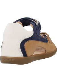 Sandalo marrone e blu con tacco bianco, realizzato in suede e pelle. Presenta chiusure a nastro e fori di ventilazione prominenti. Marchio GEox.