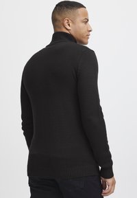 Black knitted sweater with a high collar, slim fit, and ribbed cuffs. Smooth texture, minimal stitching details, and side slits at the hem.