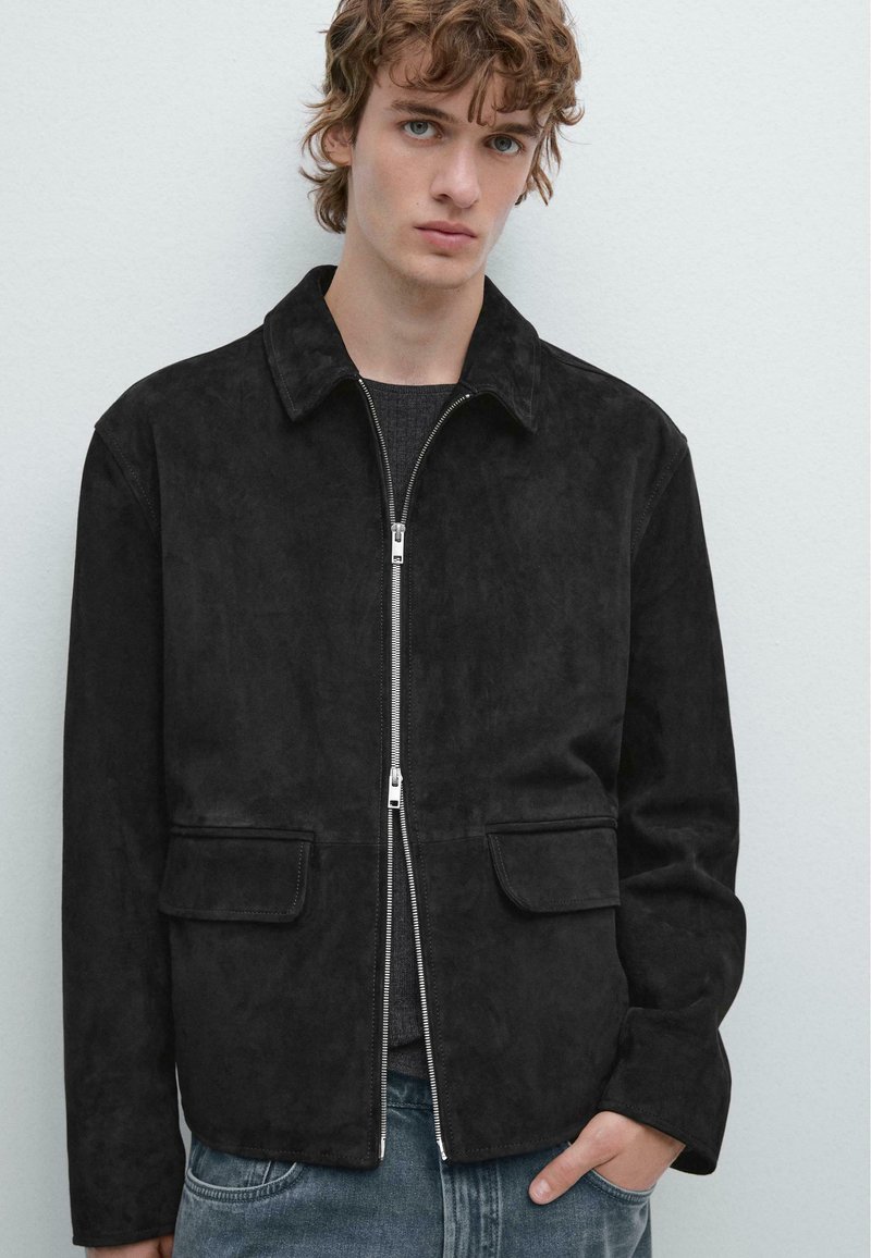 Zwarte suède jas met een kraag, ritssluiting aan de voorkant en twee opgestikte zakken. Glad texture en gestructureerde pasvorm, gecombineerd met casual jeans.
