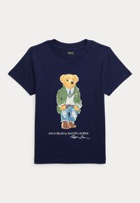 Námořnické bavlněné tričko s grafikou medvěda v zelené bundě, bílé košili a modrých džínech, s textem "Polo Bear od Ralpha Laurena".