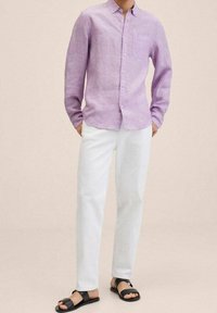Chemise en lin violet clair à boutons avec une poche poitrine, associée à un pantalon blanc et des sandales noires à enfiler. Design simple, coupe décontractée.