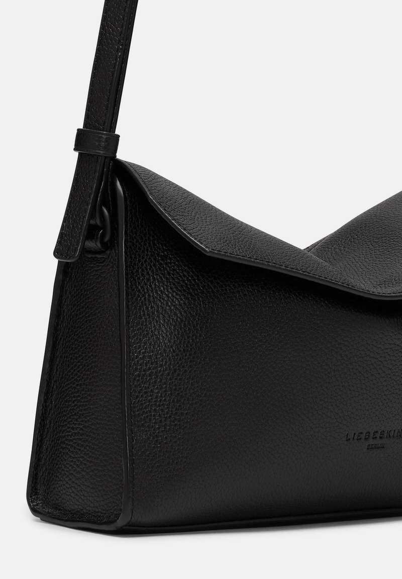 Schwarze Lederhandtasche mit strukturierten Oberflächen, dreieckigem Klappverschluss und verstellbarem Schultergurt. Hat eine minimalistische Markenpräsentation an der Seite.