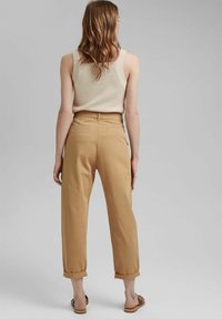 Pantaloni beige a gamba larga con orli arrotolati, realizzati in tessuto liscio, dotati di tasche posteriori e vita alta. Indossati con un top leggero.