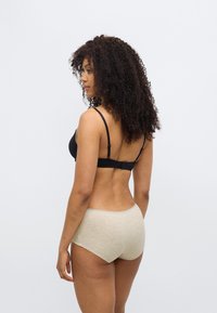 Μαύρο σουτιέν με ρυθμιζόμενους ιμάντες, σε συνδυασμό με ανοιχτό μπεζ ψηλόμεσο εσώρουχο, με λεία υφή και δαντέλα στη μέση.