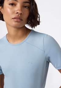 Jasnoniebieska koszulka sportowa z krótkim rękawem, gładka w dotyku, z dyskretnym logo na piersi. Zaprojektowana z myślą o komforcie i elastyczności.