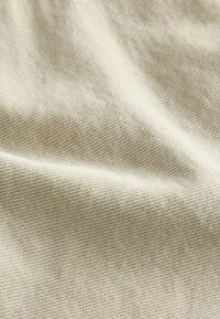 Beige textiel met een fijne, geweven structuur. Het oppervlak is glad met een subtiele glans, en toont natuurlijke vezels en lichte kleurnuances.