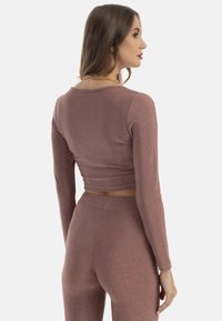 Rózsaarany, hosszú ujjú cropped top, testhezálló szabással. Puha, texturált anyag, enyhe fényességgel. Kerek nyakkivágással és rugalmas derékrésszel rendelkezik.