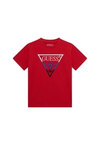 Punainen puuvillainen t-paita lyhyillä hihoilla, jossa on sinisestä ja hopeasta koostuva kolmion muotoinen logohyödyntö, jossa lukee "GUESS" ja kysymysmerkki.