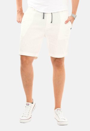 White linen shorts with elastic waistband and drawstring, side pockets, and a relaxed fit, paired with white sneakers.