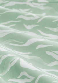 Light green fabric featuring a wavy white pattern, with a smooth texture and a soft drape, ideal for textiles and upholstery.