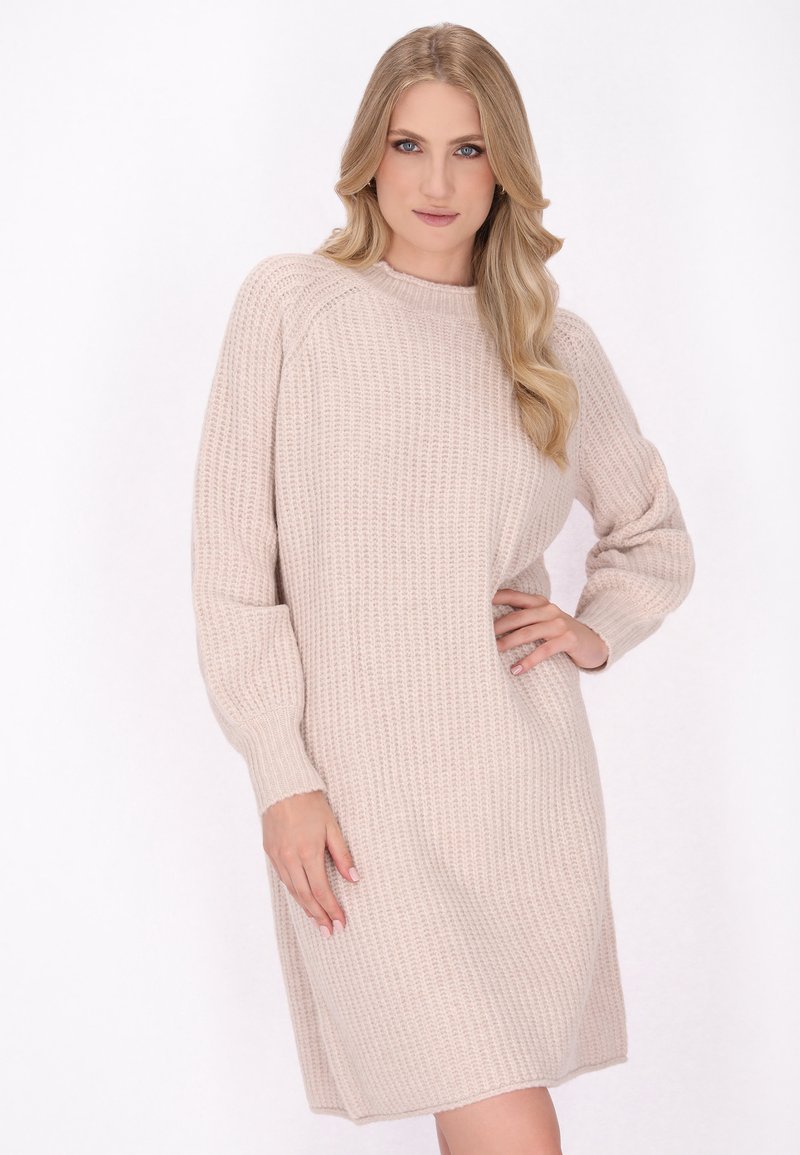 Gebreide jurk in lichtbeige, met een gestructureerd, ribbelachtig ontwerp, lange mouwen en een ontspannen pasvorm die tot halverwege de dij valt.