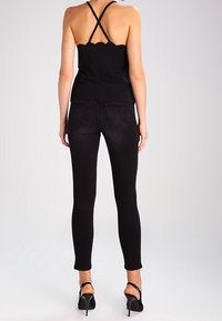 Mustassa, aaltoilevassa hihattomassa yläosassa ohuilla hihnoilla, yhdistettynä mustiin kapealahkeisiin farkkuihin. Asussa on tyylikäs siluetti ja sileä kangaspinta.