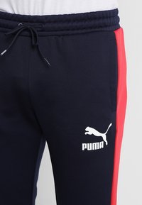 Marineblauwe sweatpants met een rode zijstripe, elastische tailleband en trekkoord. Voorzien van een wit Puma-logo op de linker dij. Zacht materiaal.