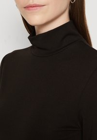 Juodas turtleneck viršus, pagamintas iš lygaus, tamprios medžiagos, pasižymintis pritaikytą dizainą ir aukštu apykakle, su švariomis linijomis ir be matomų raštų.
