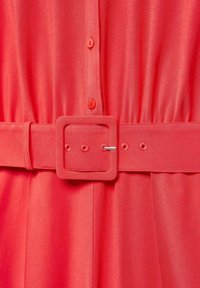 Robe corail avec devant à boutons, taille élastique et ceinture carrée assortie avec un accent métallique argenté. Tissu lisse et léger.
