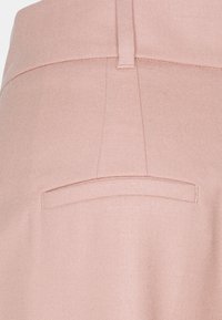 Närbild av skräddarsydda rosa byxor som visar sömmarna på bakfickan och detaljerna på bältesöglan.