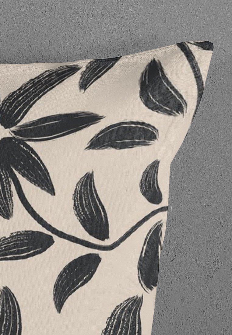 Cuscino beige con un motivo di vite nera a foglie contro uno sfondo di muro grigio texture.