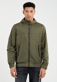 Alyvuogių žalios spalvos lengvas džemperis su kapišonu, priekinė užtrauktuku ir juodais akcentais. Yra elastingi rankogaliai ir dvi šoninės kišenės. Lygi tekstūra.