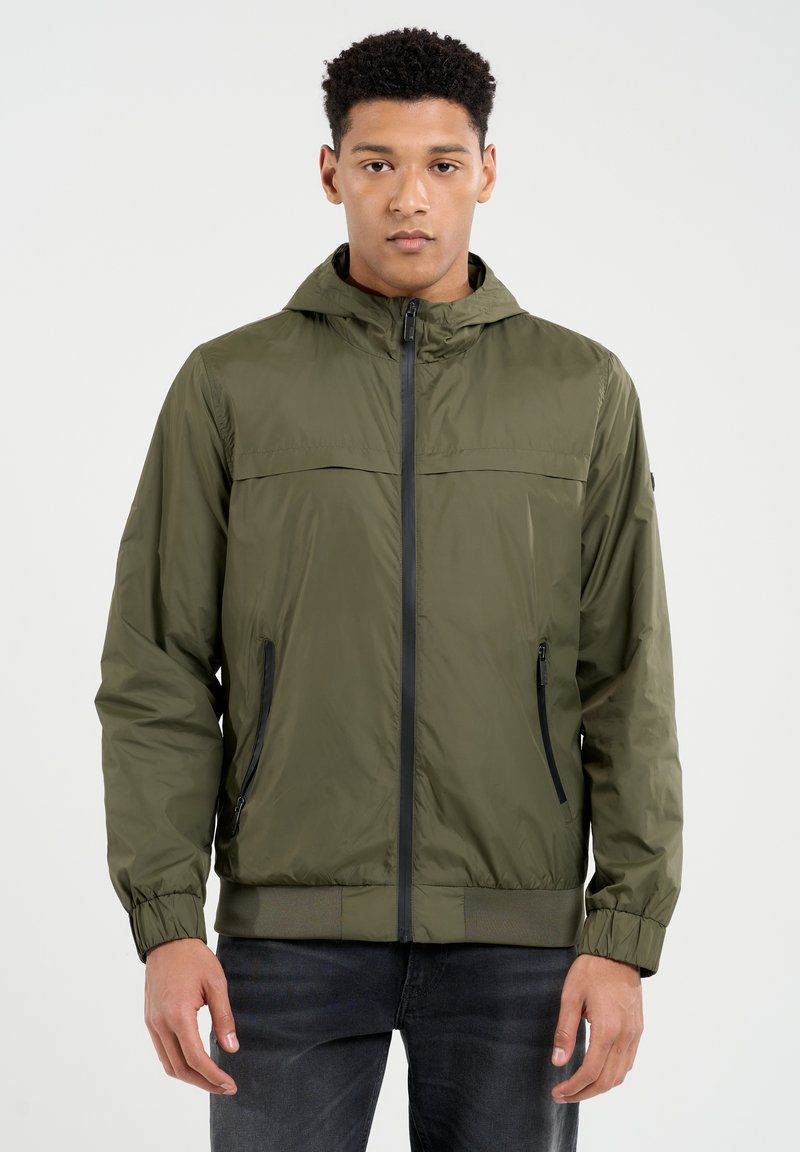 Alyvuogių žalios spalvos lengvas džemperis su kapišonu, priekinė užtrauktuku ir juodais akcentais. Yra elastingi rankogaliai ir dvi šoninės kišenės. Lygi tekstūra.