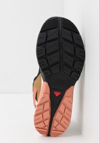 Scarpa sportiva nera e rosa con una suola in gomma testurizzata, caratterizzata da battistrada profondo e una sezione superiore beige a contrasto.