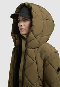 Olivgrüne gesteppte Jacke mit großer Kapuze,Frontreißverschluss und schwarzen Akzenten. Hat eine glatte Textur und ein Rautenmuster auf dem Stoff.