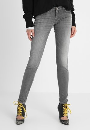 Person trägt ausgebleichte graue Skinny-Jeans, kombiniert mit schwarzen High Heels mit leuchtend gelben Schnürsenkeln und einem schwarzen Langarmoberteil.