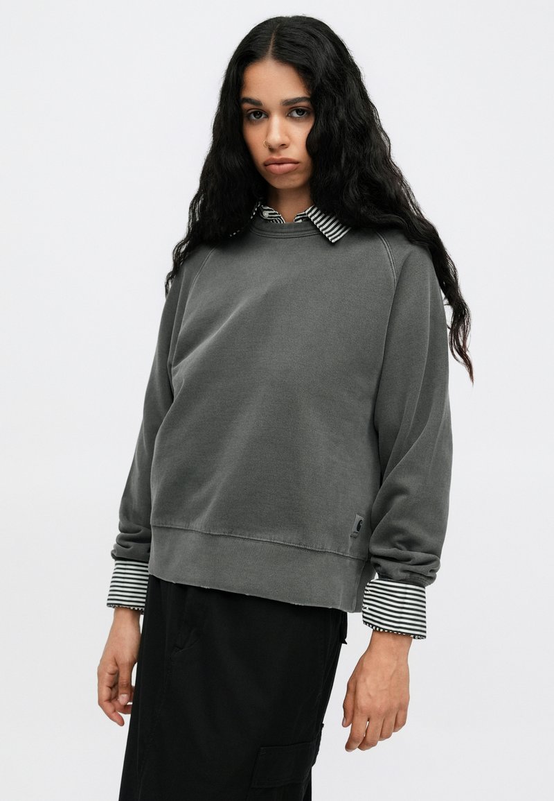 Sudadera gris con un corte relajado, puños acanalados con un patrón de rayas en blanco y negro. Logo bordado en el dobladillo. Tejido texturizado.