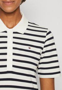 Polo a righe bianco e blu navy, con colletto classico, patta con bottoni e piccolo logo sul lato sinistro. Tessuto di cotone comodo.