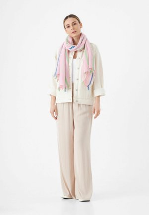 Écharpe rose pastel avec des accents verts et bleus, superposée à une veste en denim blanche et un pantalon large de couleur crème, sur fond blanc.