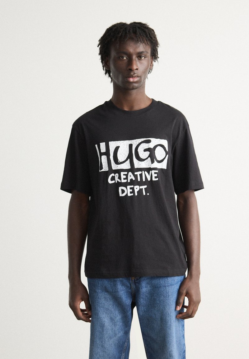 Black cotton t-shirt featuring bold white text "HUGO CREATIVE DEPT." on the front, complemented by relaxed-fit blue denim jeans.