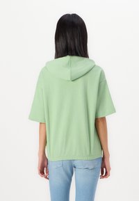 Muntgroene capuchontrui met korte mouwen, een ronde onderkant en elastische tailleband. Gemaakt van zachte, lichte stof.