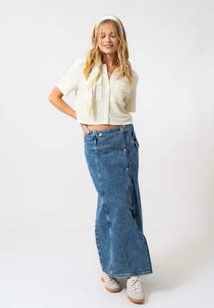 Hvit teksturert crop top med korte ermer, satt sammen med et langt blått denimskjørt med knapper på siden og beige joggesko.