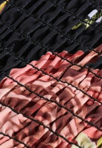 Ekranowany materiał w różnorodnych odcieniach różu i ziemistych tonów, otoczony czarnymi elastycznymi szwami, tworząc teksturowane fałdy.