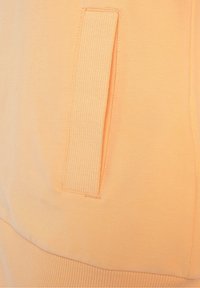 Felpa color pesco con tasca a coste e tessuto testurizzato, finitura liscia e cintura elastica nella parte inferiore.