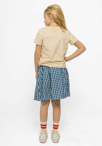 Camiseta de algodón beige, falda de cuadros azul y blanca con pliegues, zapatillas blancas y calcetines a rayas rojas, vista desde atrás.
