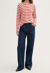 Rot-weiß gestreiftes Langarmshirt kombiniert mit dunkelblauen, weit geschnittenen Jeans und schwarzen spitzen Schuhen. Einfaches Design, bequemer Sitz.