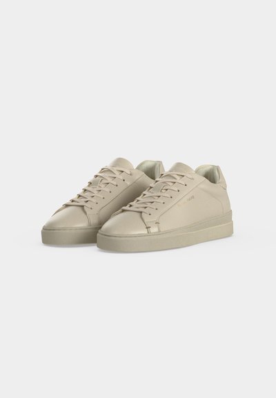 Ζευγάρι μπεζ χαμηλά sneakers με κορδόνια και μίνιμαλ σχέδιο σε απλό ανοιχτό φόντο.